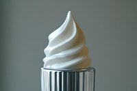 Creamy white soft serve ice cream swirled in classic spiral shape atop metallic striped container against neutral background, showcasing smooth texture and form.