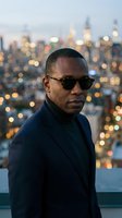 African American male wearing dark sunglasses and navy blazer against illuminated city skyline at dusk. Urban lifestyle and fashion portrait.