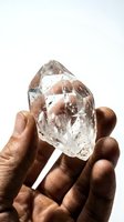 Dark-skinned male hand holding a large clear quartz crystal point against white background, showcasing natural mineral beauty for wellness and spirituality.