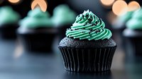 Dark chocolate cupcake with mint green frosting swirl topped with silver sprinkles on blurred background. Macro food photography with soft bokeh lights creates festive mood.