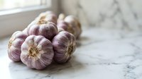 Fresh purple garlic bulbs with papery skin arranged on marble surface near window, suitable for food photography, culinary content, and healthy cooking themes.