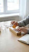 Adult hands pouring medication from amber bottle into wooden organizer at table with water glass and notebook, depicting daily supplement routine and healthcare management.