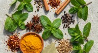 Fresh mint leaves with aromatic spices including star anise, cinnamon, turmeric powder, peppercorns and coriander seeds arranged on textured surface for cooking.