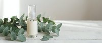Natural skincare serum bottle with eucalyptus leaves on white wooden surface for organic beauty and wellness spa treatments.