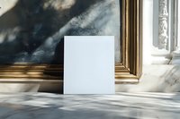 Blank white square card standing on marble surface with dramatic natural sunlight and shadows casting through window, gold frame in background.