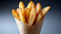 Crispy golden potato wedges served in brown paper cone against dark background, close up view showing texture and seasoning of freshly cooked french fries.