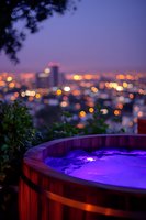 Hot tub with purple LED lighting on rooftop terrace overlooking blurred city lights at dusk, creating romantic ambiance with bokeh effect in background.