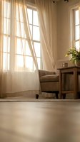 Cozy living room interior with armchair near window with flowing curtains and warm sunlight creating peaceful atmosphere for home decor and relaxation.