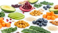 Colorful assortment of fresh superfoods including avocado, berries, nuts, seeds and vegetables arranged on white background for healthy eating concepts.