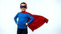 Young Caucasian boy in superhero costume with red cape and mask posing confidently on white background for children's play and imagination concepts.