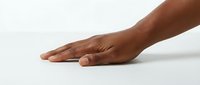 Close-up of an open hand with medium-dark skin tone resting on a white surface, showing palm and fingers extended in a calm, welcoming gesture for healthcare, wellness, or support concepts.