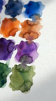 Vibrant watercolor paint blots in blue, orange, purple and green hues on white paper texture. Abstract artistic background for creative projects and designs.