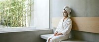 Young Asian woman in white bathrobe and towel relaxing in modern spa bathroom with bamboo view, wellness and self-care lifestyle concept.
