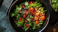 Fresh mixed green salad with cherry tomatoes, pine nuts and quinoa in dark ceramic bowl on moody background, healthy vegetarian lunch bowl.
