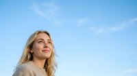 Mature blonde woman with fair complexion gazing upward against clear blue sky, expressing hope and optimism for wellness, lifestyle and inspirational content.