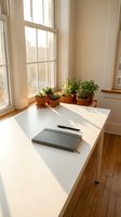 Minimalist home office workspace with white desk, notebook, pen and small potted plants on windowsill in natural sunlight for productivity and remote work.