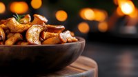 Fresh roasted mushrooms with herbs in wooden bowl against dark background with warm bokeh lights, close up view of seasonal autumn appetizer.