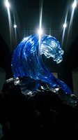 Blue glass wave sculpture with dramatic lighting on dark rocks creating artistic ocean motion display for modern interior design and contemporary art concepts.