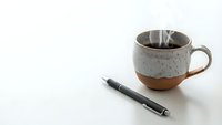 Ceramic coffee mug with steam and black pen on clean white surface for morning productivity and workspace concepts.