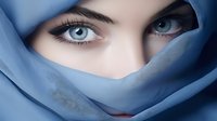 Mysterious blue eyes peek through soft blue fabric veil, creating dramatic contrast with long eyelashes and defined brows. Artistic fashion portrait captures enigmatic gaze.