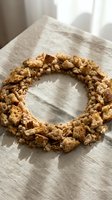 Homemade granola wreath made with oats, nuts, and dried fruits arranged in circular shape on natural linen fabric with soft window light.
