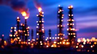 Defocused industrial refinery lights glowing at twilight with dramatic blue sky, creating abstract bokeh effect of illuminated manufacturing facility at dusk.