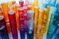 Colorful laboratory test tubes filled with vibrant liquids in orange, pink, red, yellow, and blue hues arranged in rows for scientific research, chemistry education, or medical testing purposes.