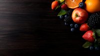 Fresh seasonal fruits arranged on dark wooden background with copy space. Oranges, apple, berries create corner composition for food photography and design.