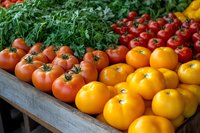 Fresh red and yellow tomatoes with green herbs displayed on wooden surface at farmers market, colorful organic produce arrangement for healthy eating.
