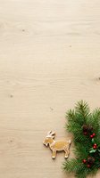 Gingerbread goat cookie with white icing sits on light wood surface next to evergreen branches, pinecones and red berries for holiday baking and festive decoration projects.