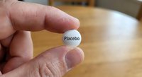 Hand holding white placebo pill tablet between fingers on wooden table background for medical research and pharmaceutical studies.