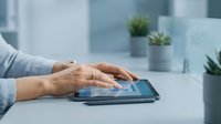 Professional businesswoman using digital tablet at modern office desk with plants in background for technology and workplace productivity concepts.