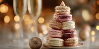Festive tower of colorful macarons with gold glitter decoration on elegant table setting with bokeh lights and champagne glasses in background.