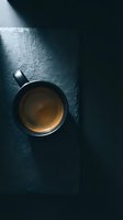 Black coffee cup on dark slate surface with dramatic lighting and shadows creating moody atmosphere for cafe and beverage concepts.