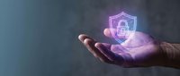 Hand holding glowing purple cybersecurity shield with lock icon representing data protection and digital security solutions for business technology.