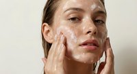 Young woman applying white facial cleanser foam with hands during skincare routine for healthy glowing skin and beauty care regimen.