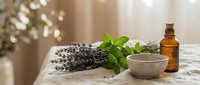 Fresh mint leaves and dried lavender flowers arranged on white marble surface with amber glass bottle and ceramic bowl for natural aromatherapy and wellness.