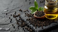 Black peppercorns scattered on dark stone surface with glass bottle of olive oil, wooden spoon, and fresh basil leaves, moody food photography setup.