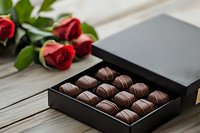 Luxury chocolate truffles in elegant black gift box with red roses on rustic wooden table. Romantic gourmet dessert setting for special occasions.