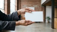 Hands holding blank white card in modern loft space with brick walls and industrial interior, suitable for business branding and corporate mockup presentations.
