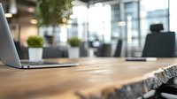 Rustic wooden desk with laptop in modern office space featuring natural light, green plants and blurred background. Workspace concept for business design.