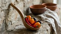 Rustic kitchen still life with fresh cherry tomatoes in wooden spoon and terracotta bowls on textured stone surface for cooking and food photography.