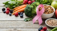 Pink ribbon with fresh vegetables, fruits, nuts and grains on wooden background promoting healthy nutrition and cancer awareness lifestyle choices.