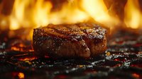 Juicy grilled beef steak with grill marks and caramelized crust cooking over hot charcoal fire with bright flames in background, close up view of meat preparation.