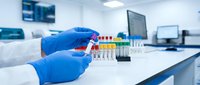 Laboratory technician in blue gloves holding test tubes with colorful samples in modern medical research facility for scientific analysis and diagnostics.