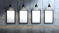 Four empty white frames illuminated by pendant lamps on concrete wall with tiled floor, modern gallery exhibition space for artwork display.