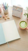 Flat lay workspace with open notebook, September calendar, colored pens, matcha latte, dried flowers and potted plant on wooden desk for planning and productivity content.