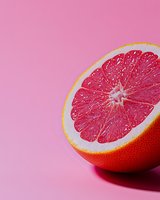 Fresh juicy grapefruit half showing vibrant pink flesh and detailed pulp texture against pink background, minimal food composition for healthy lifestyle concept.