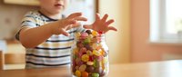Young child reaching for colorful candy jar on kitchen counter, temptation and sweet treats concept for parenting and nutrition education materials.