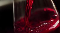 Red wine pouring into glass with dynamic splash and motion, rich burgundy color against dark background creates dramatic luxury beverage photography.